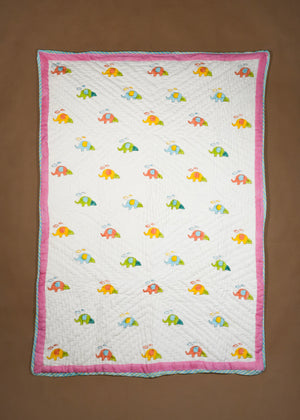 A baby quilt with a white background, featuring a repeating pattern of colorful elephants and a pink border, laid flat on a brown background.
