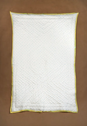 A white quilted baby quilt with blue dots and a yellow and white twisted rope border, laid flat on a brown background.