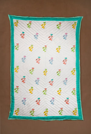 A rectangle white quilted blanket featuring a repeating pattern of colorful dancing figures and a bright teal border, displayed flat against a solid brown background.