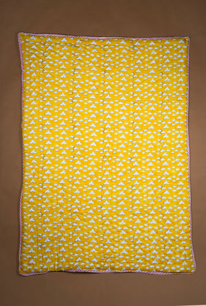 A rectangle yellow quilt, featuring a repeating white cloud and a thin orange border, laid flat against a solid brown background.