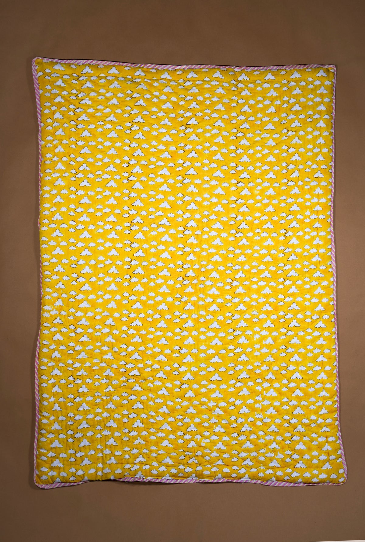 A rectangle yellow quilt, featuring a repeating white cloud and a thin orange border, laid flat against a solid brown background.