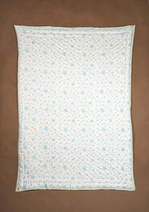 A rectangle white quilted blanket with a light blue star pattern, laid flat on a solid brown background.