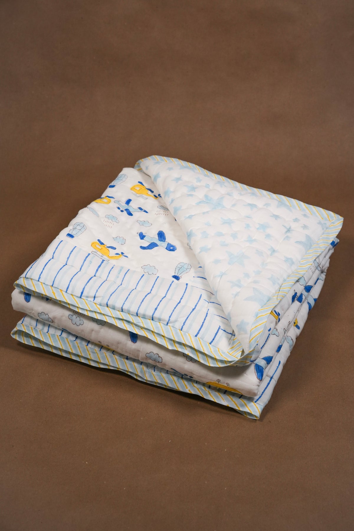 folded baby qulted blanket with aeroplane and helicopter on front and light blue star motif on back.