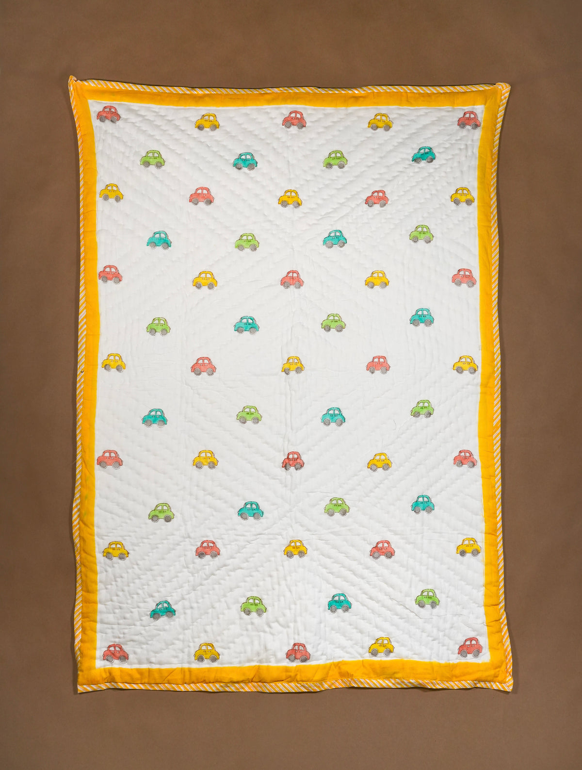 A baby quilted blanket with a white center, colorful embroidered cars, and a bright yellow border, laid flat on a brown background.